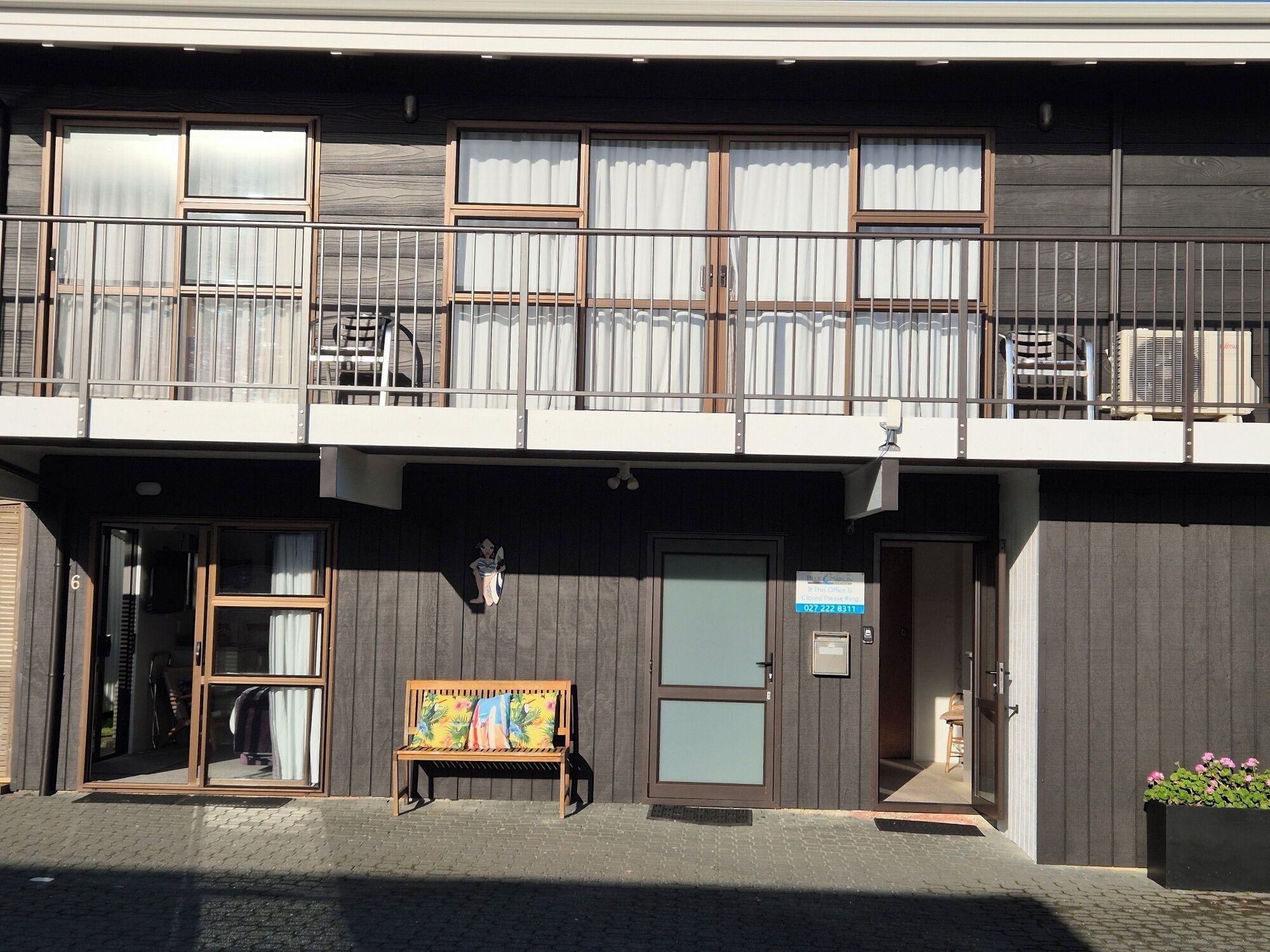 Un edificio a due piani con un balcone, una panchina con un quadro e un'insegna che indica un ufficio commerciale.
