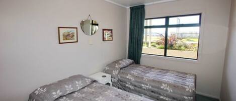 A room with two beds, a small bedside table, a window with a view of the outdoors, and a ceiling light.