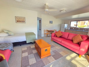 Une pièce comprenant un lit, un canapé rouge, une commode en bois, une table à manger avec des chaises et un coin cuisine.