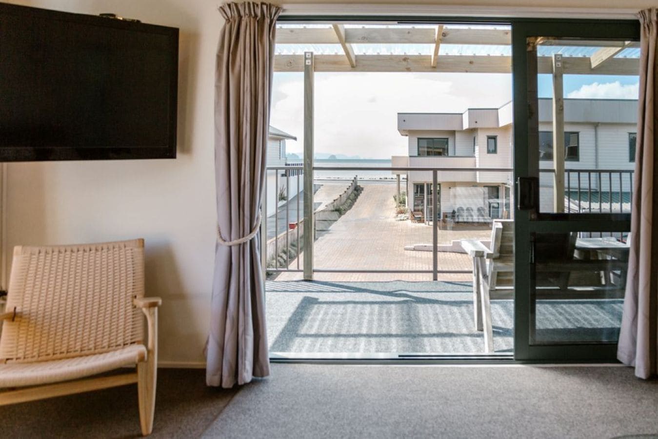 A room with a view of a beach, a wicker chair, and a table with chairs.