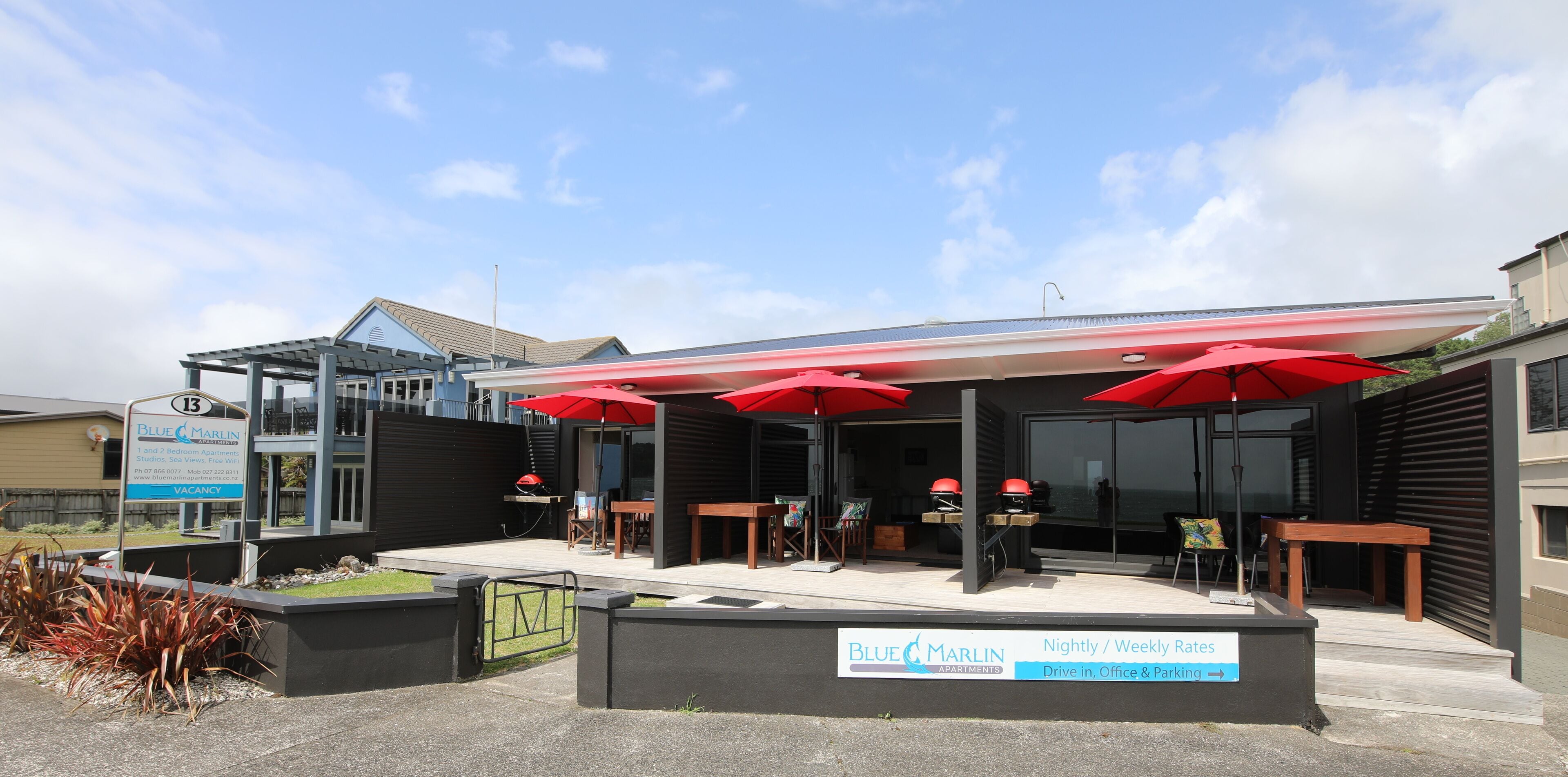 A Blue Marlin Apartments building with a covered outdoor seating area, red umbrellas, and a sign indicating nightly and weekly rates.