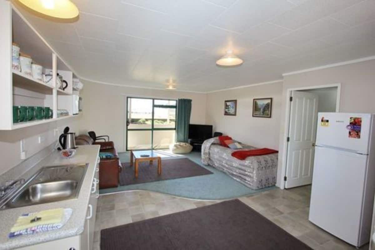A compact living space with a kitchenette, a sofa, a television, and a door leading to another room.