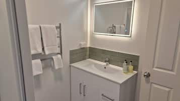 Une salle de bain avec un lavabo blanc, un miroir et un porte-serviettes sur lequel sont disposées plusieurs serviettes.