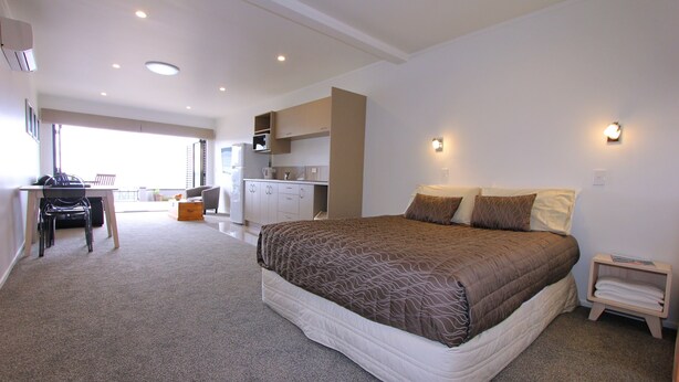 Een slaapkamer met een groot bed, een bureau en een kitchenette op de achtergrond.