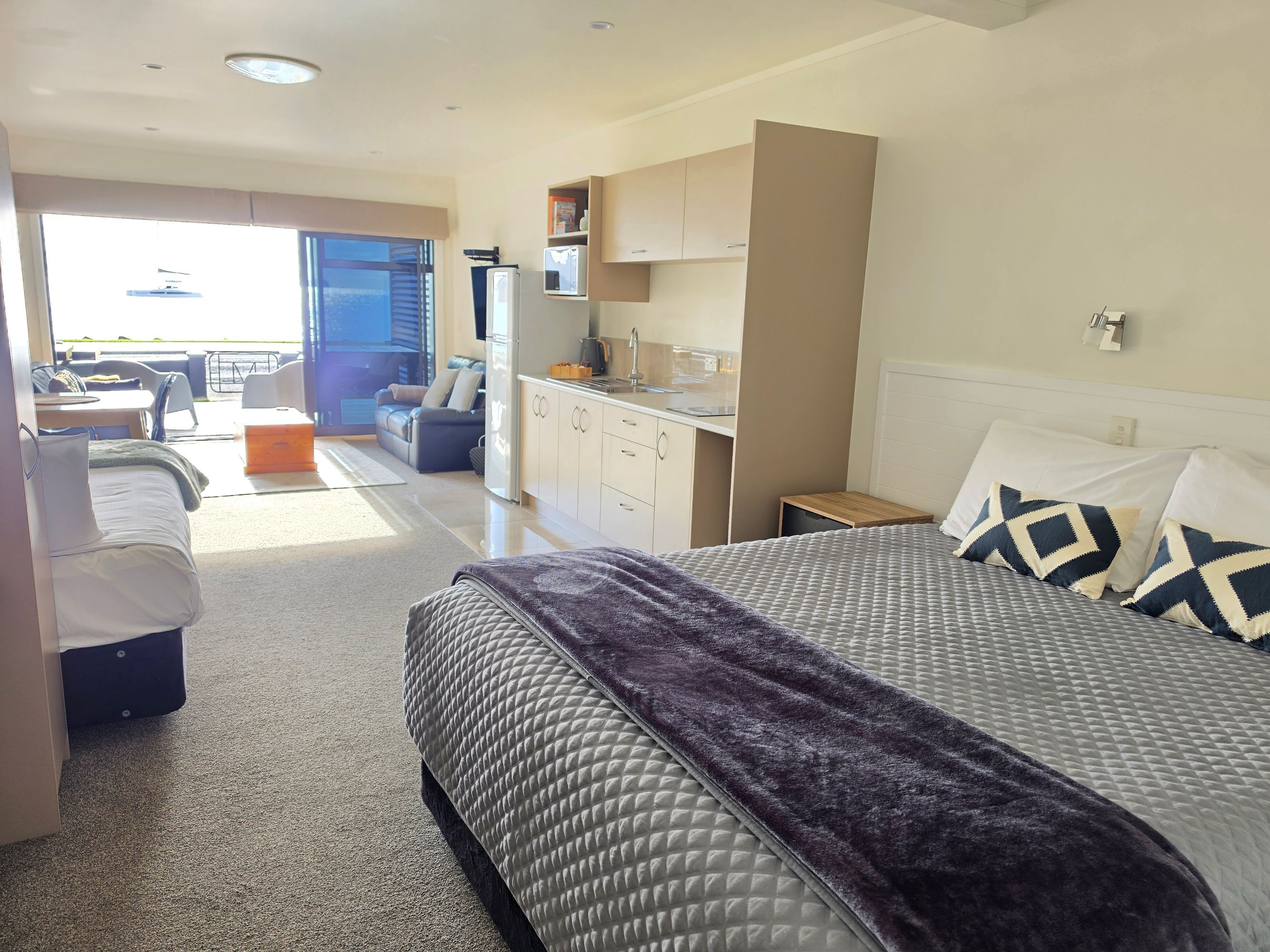 Habitación de hotel con cama, kitchenette, zona de estar con mesa y sillas, y balcón con vistas.