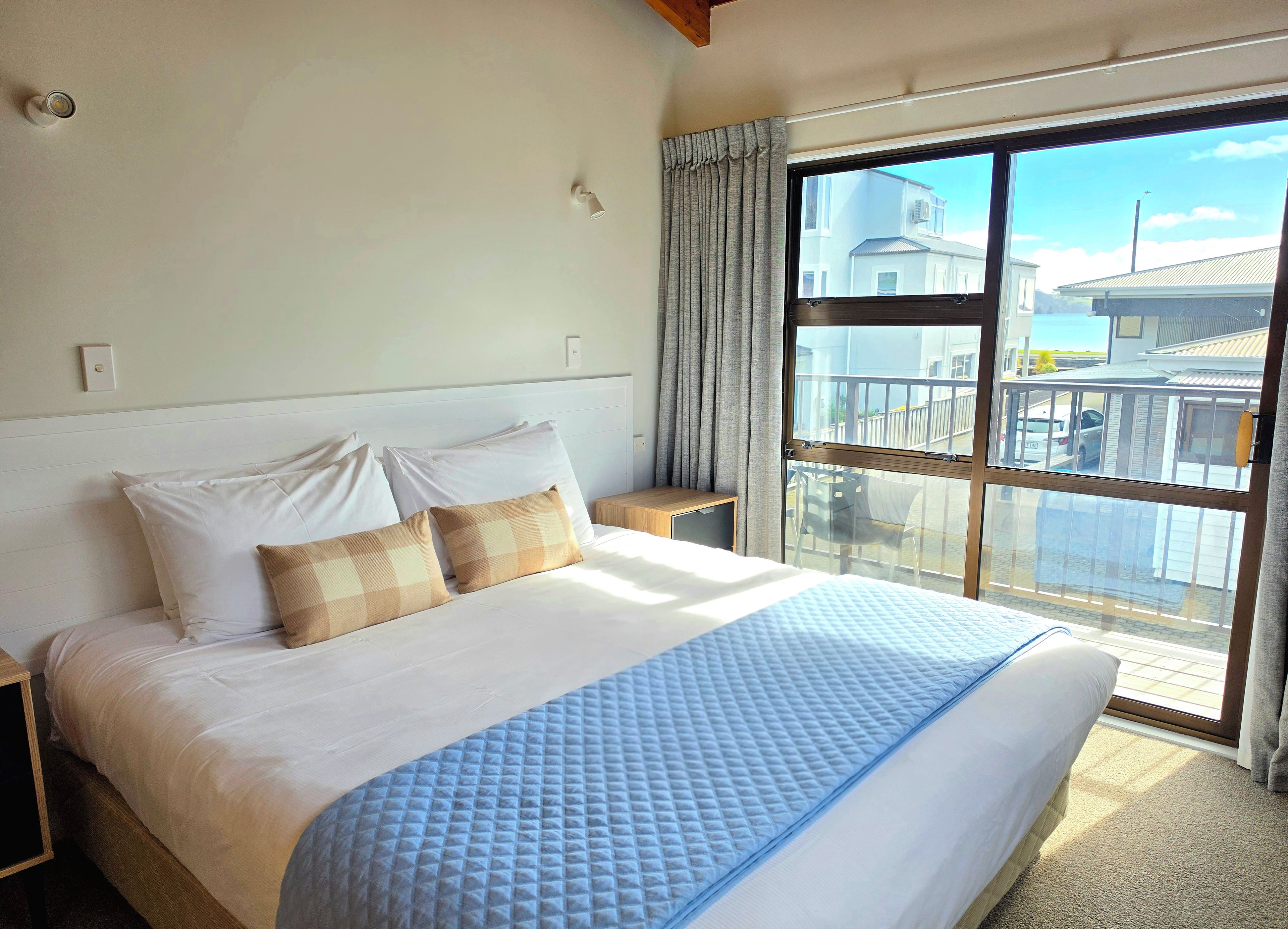 A hotel room with a large bed, a nightstand, a window with a view of buildings, and a curtain.