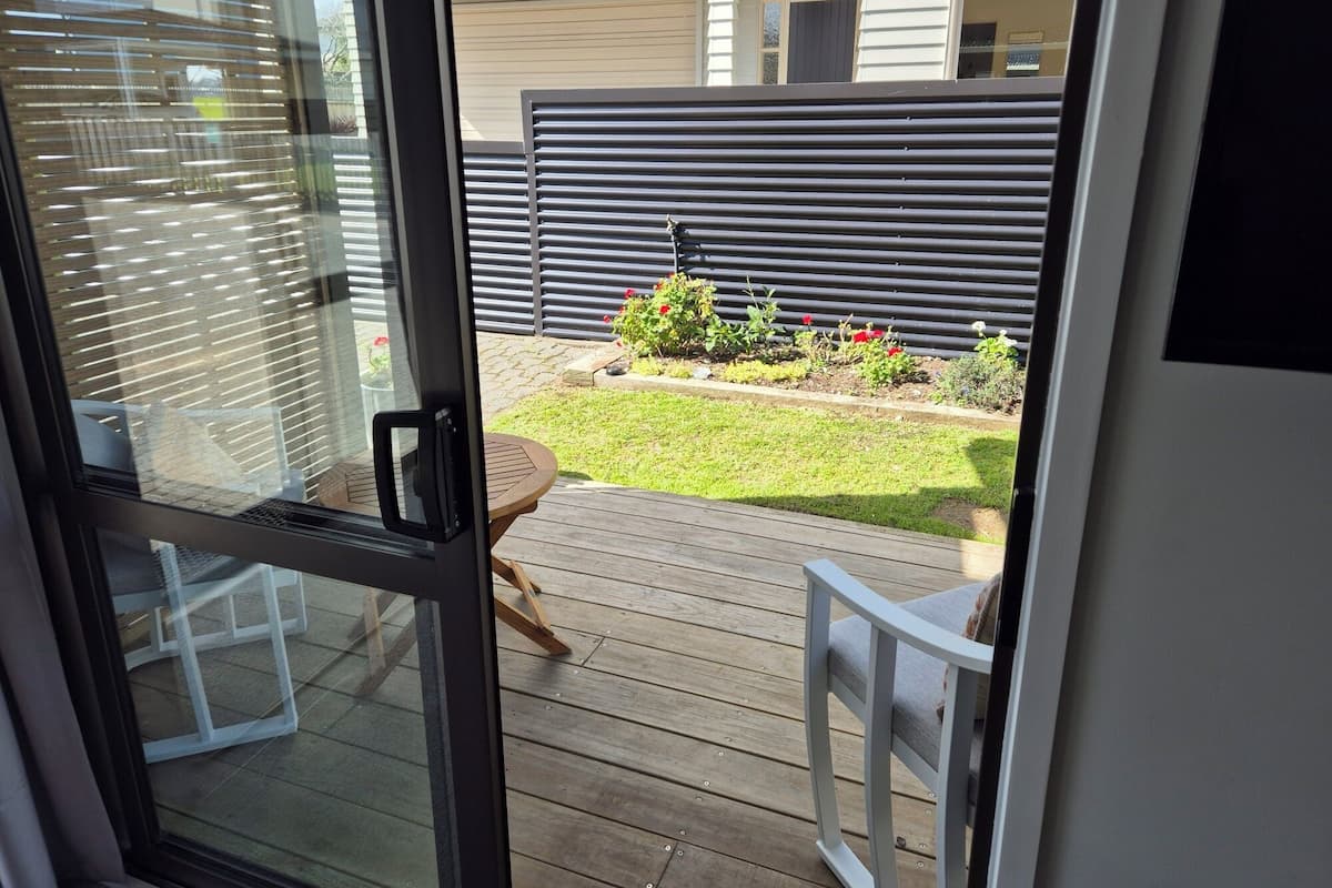 A view from a sliding glass door into a patio area with a wooden deck, a small round table, and a white chair.