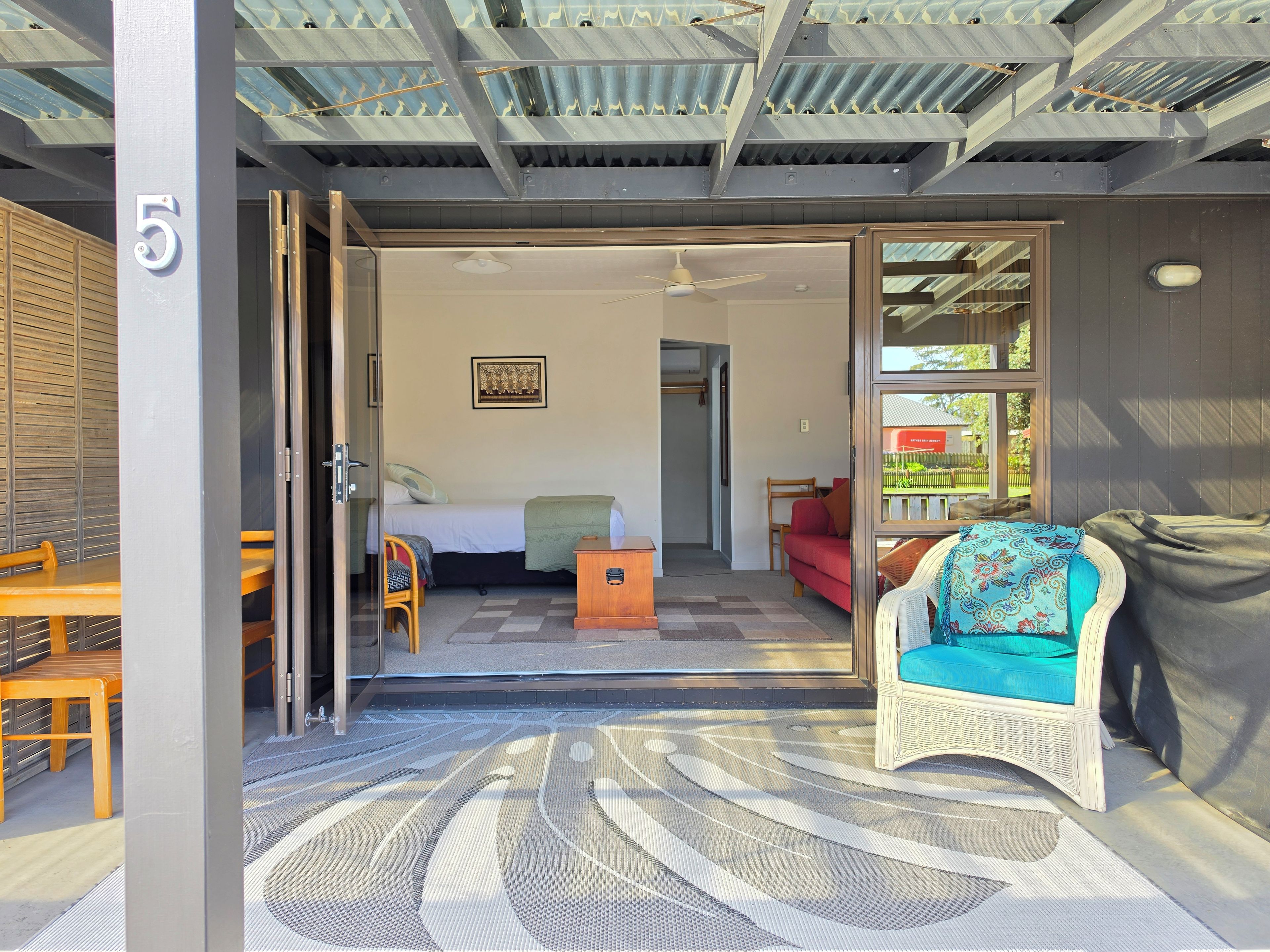 A room with a bed, a chair, a small table, and a door leading to another room.