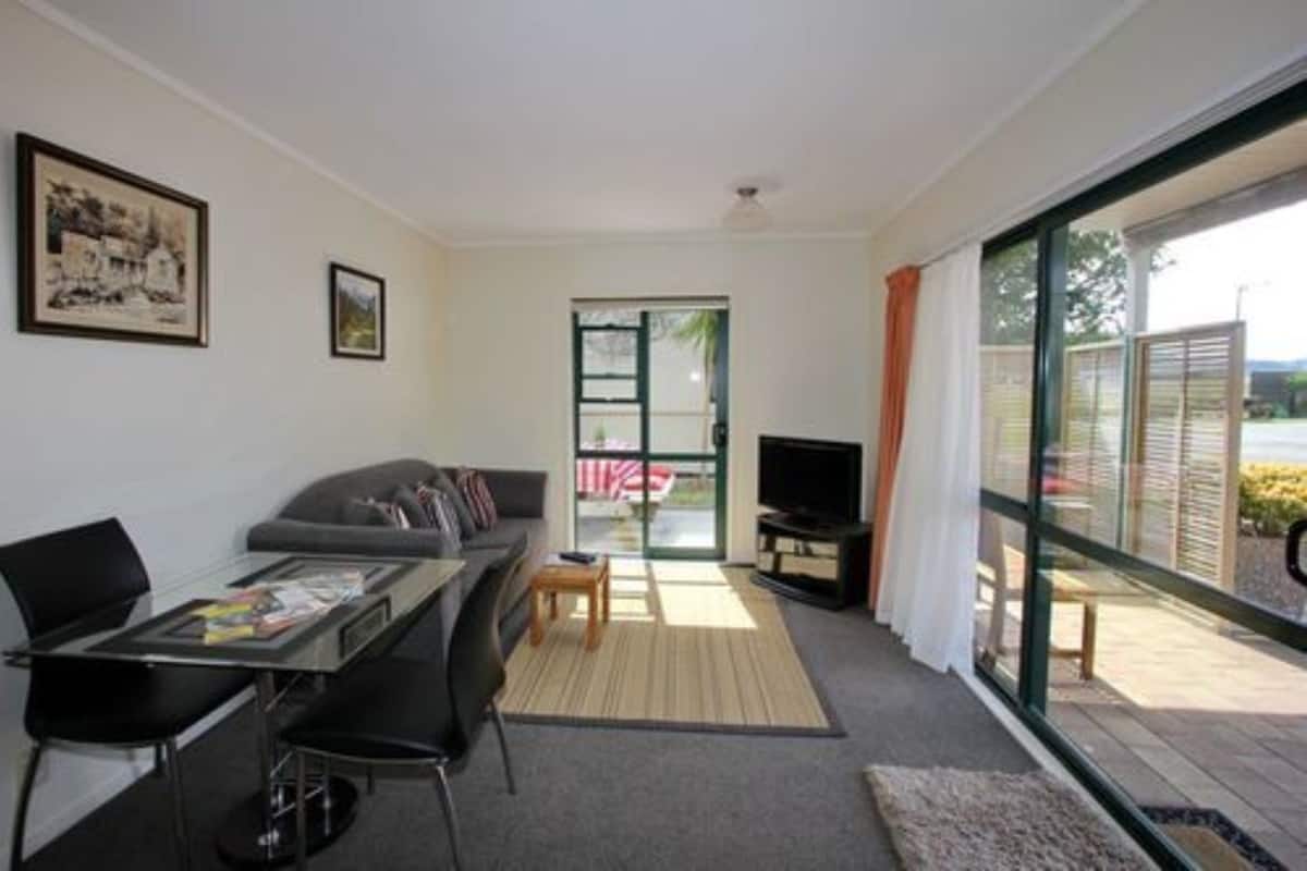 A modern living room with a sofa, a glass dining table, a TV, and a sliding glass door leading to an outdoor area.