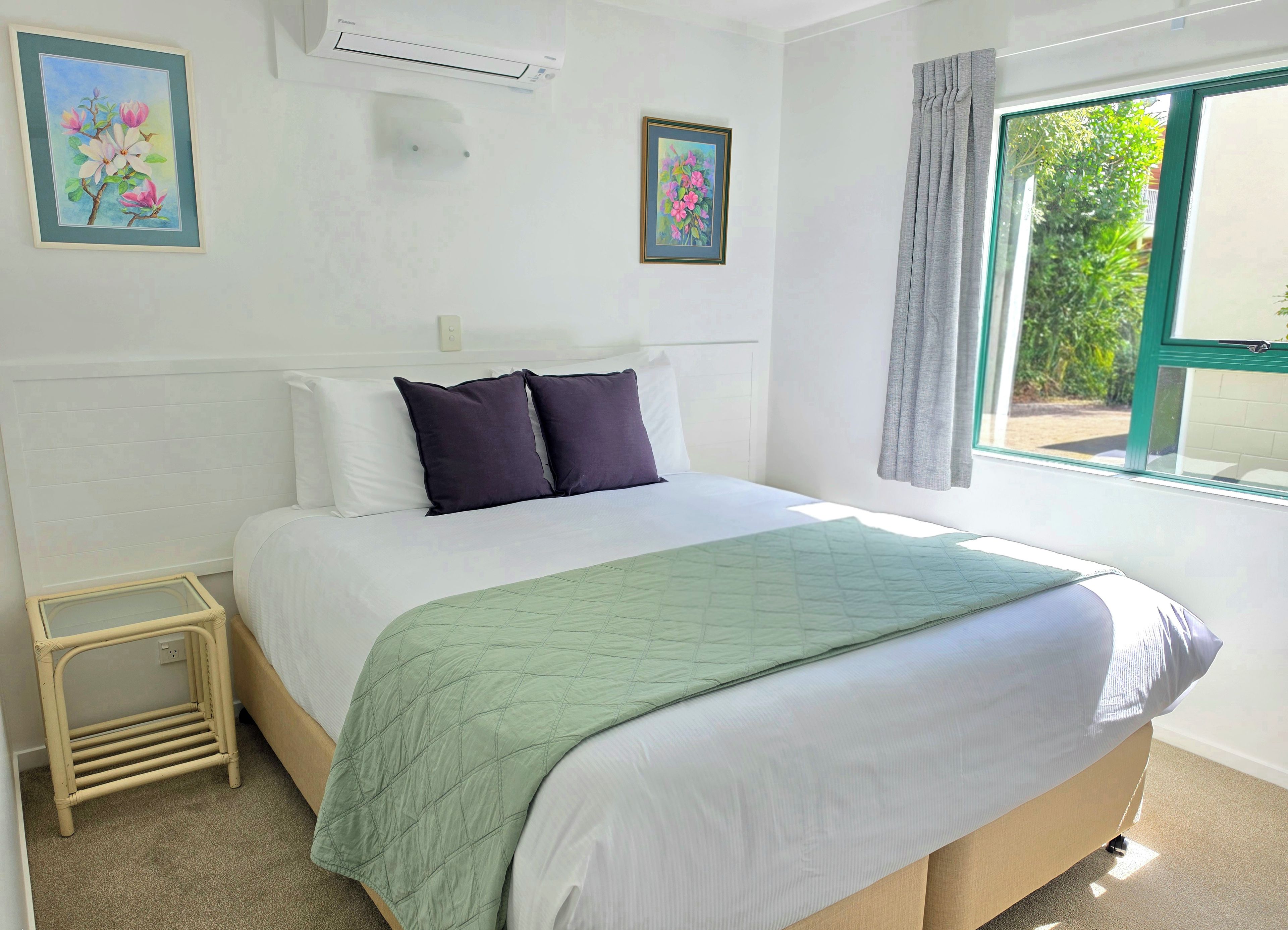 Un dormitorio con una cama, una ventana y dos cuadros con motivos florales.
