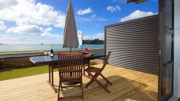 Une terrasse en bois avec une table et des chaises, d’où l’on peut admirer un plan d’eau et une île lointaine.