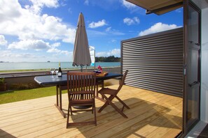 Eine Holzterrasse mit Tisch und Stühlen, mit Blick auf ein Gewässer und eine entfernte Insel.