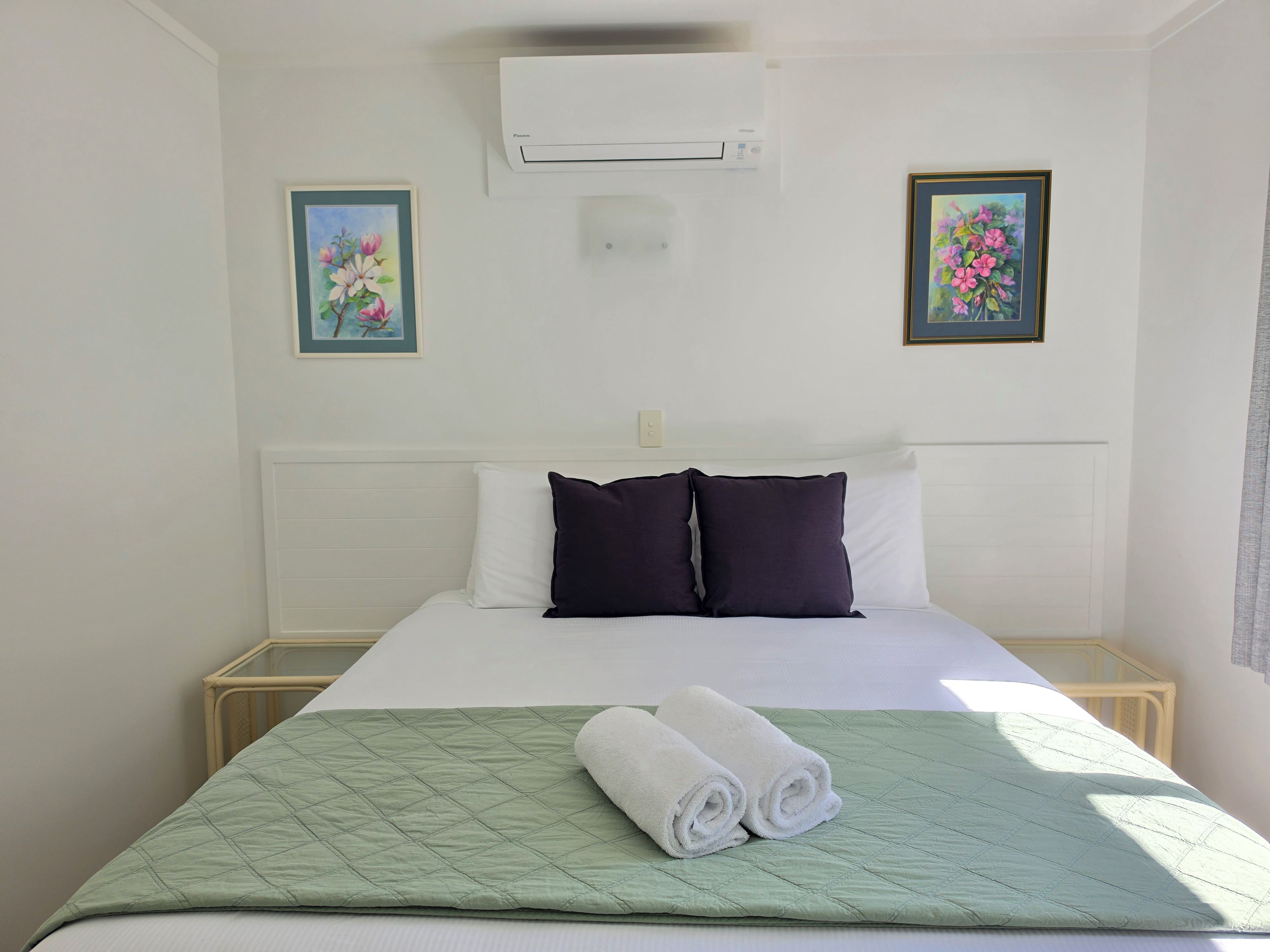 A hotel room with a bed, two pillows, a green quilt, and two rolled towels.