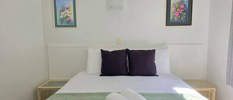 A hotel room with a bed, two pillows, a green quilt, and two rolled towels.
