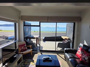 A modern living room with a view of the sea, a sofa, a coffee table, and a chair. - Blue Marlin Apartments (Whitianga)
