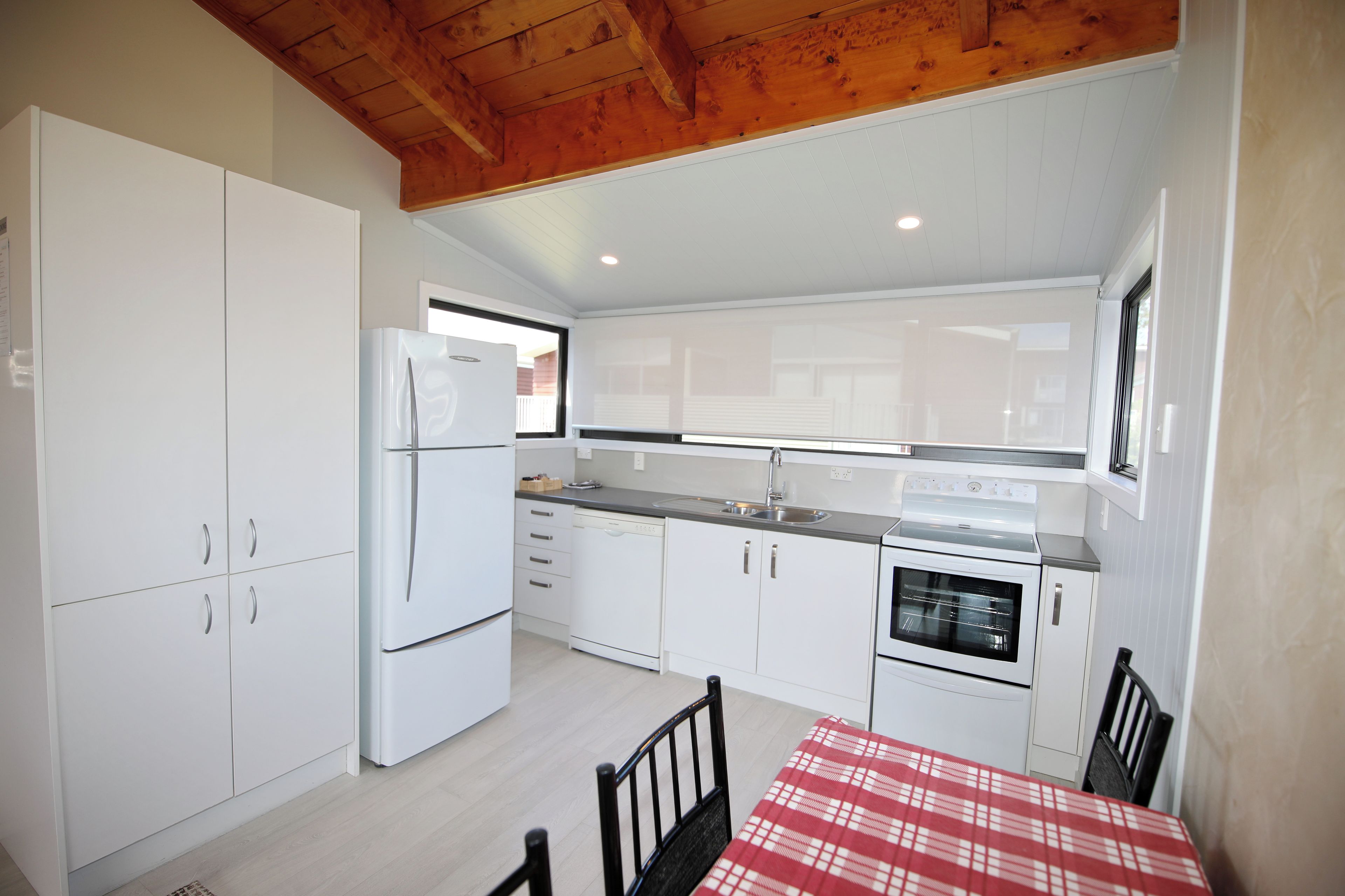 Une cuisine compacte avec des meubles blancs, un réfrigérateur, un lave-vaisselle, un four et une table à manger avec des chaises.