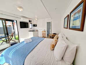 Ein Schlafzimmer mit Bett, einer kleinen Küchenzeile, einem Essbereich und Blick durch eine Glastür.