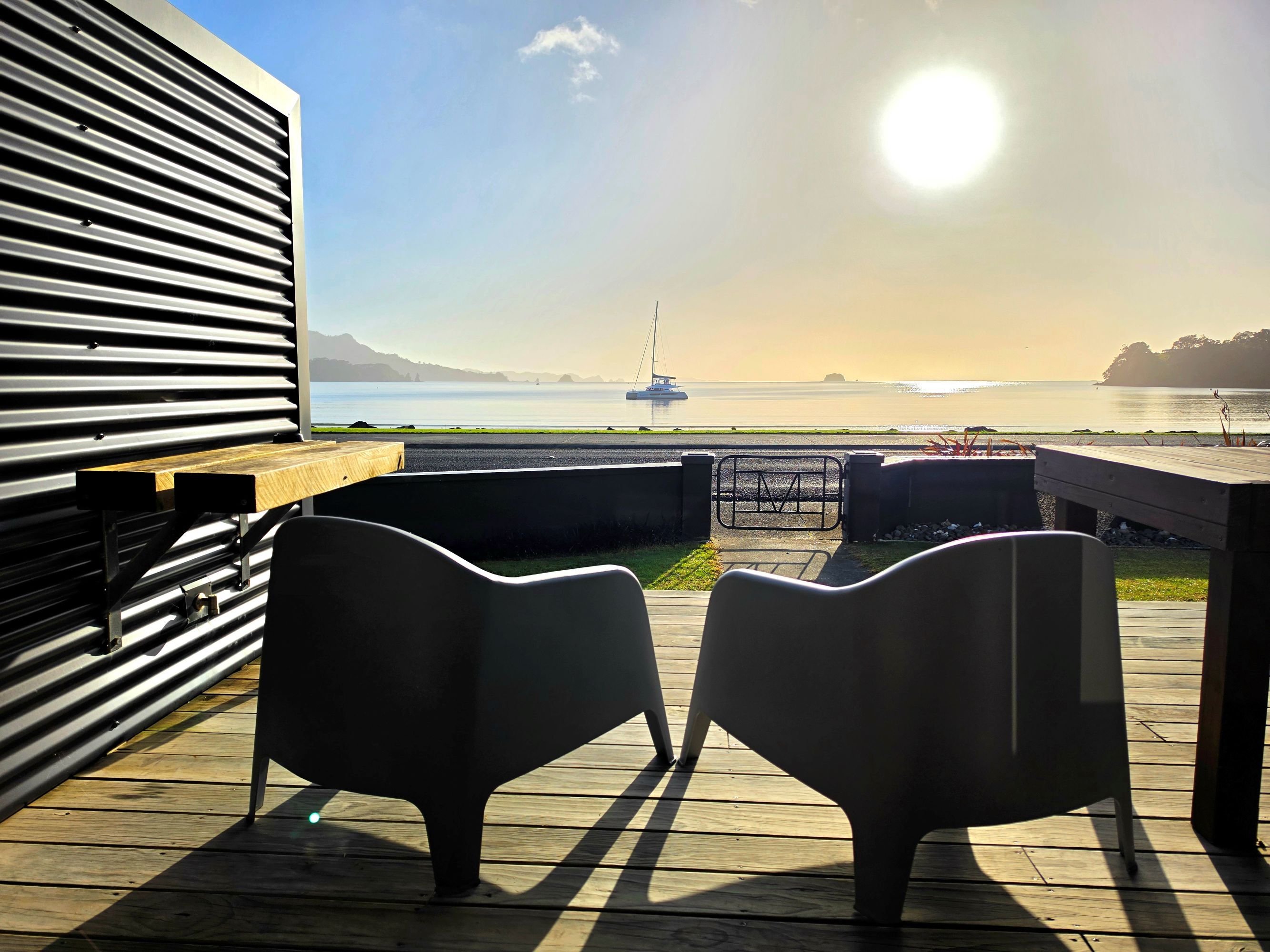 A deck with two chairs facing a view of a calm body of water and a sailboat.