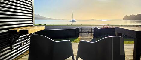 A deck with two chairs facing a view of a calm body of water and a sailboat.