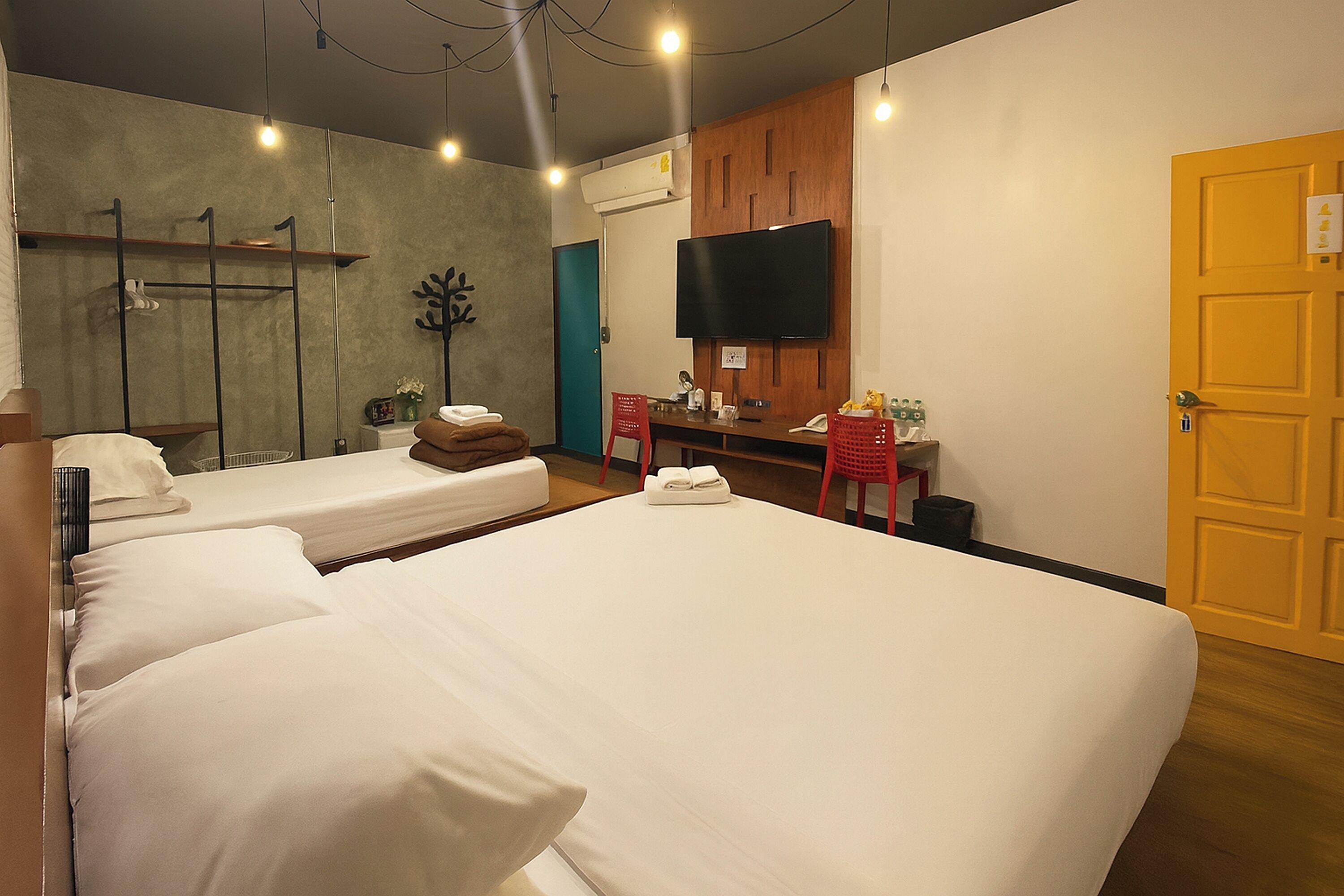 A hotel room with three beds, a desk with a chair, a flat-screen TV, and a wooden door.