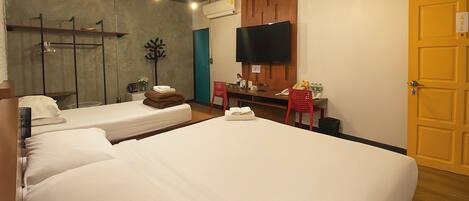 A hotel room with three beds, a desk with a chair, a flat-screen TV, and a wooden door.