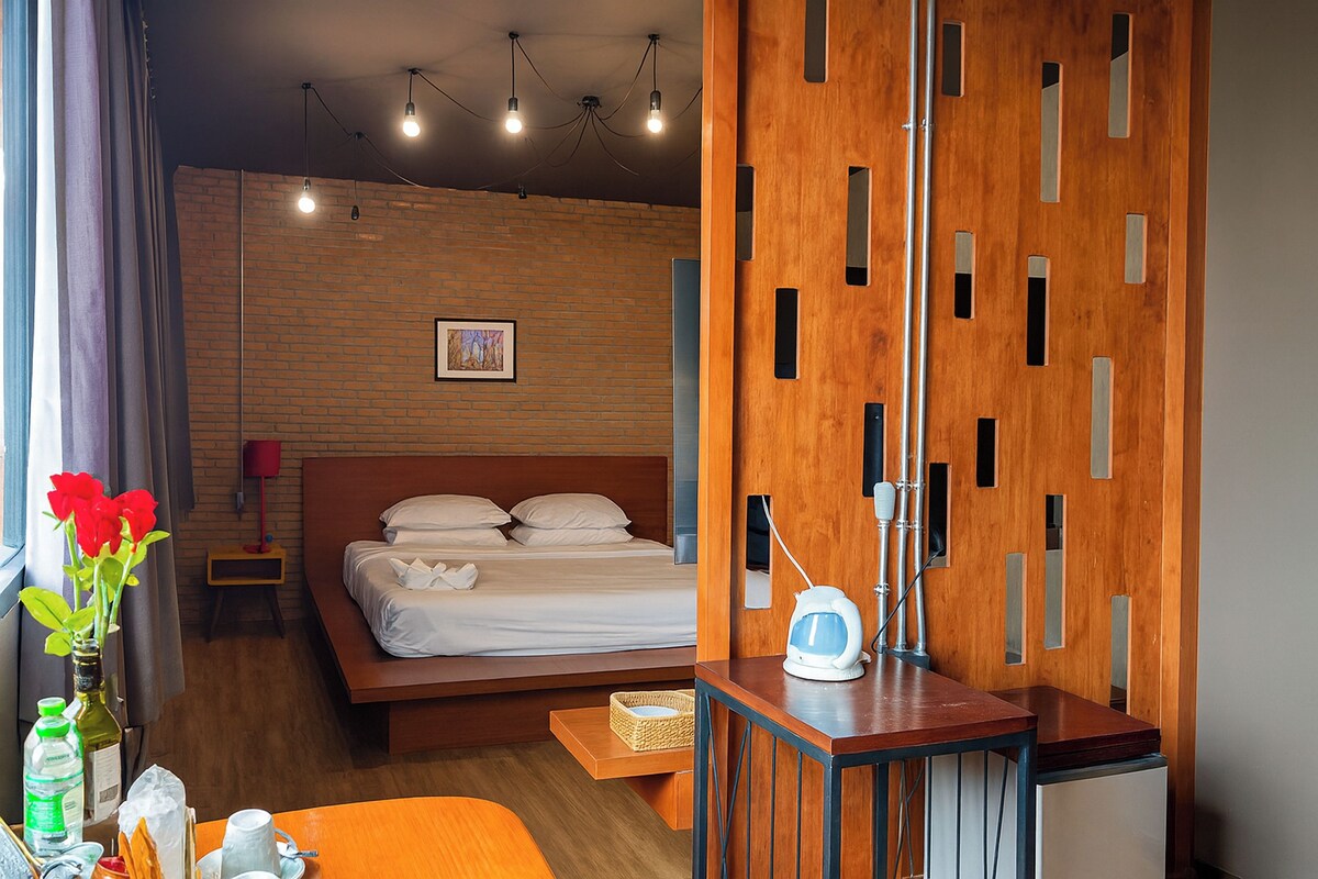 Habitación de hotel moderna con una cama de madera, un escritorio con una lámpara y vistas de la ciudad.