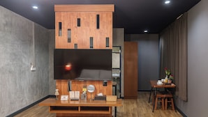 A modern living room with a flat-screen TV mounted on a wooden console, a dining area with a table and chairs, and a kitchen area in the background. - The Loft Room Nimman (Chiang Mai)