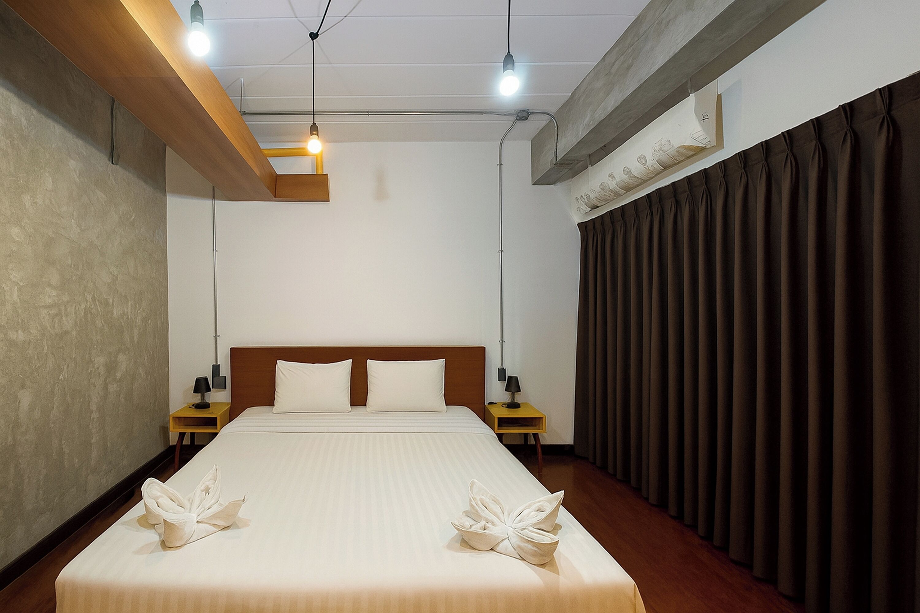 A hotel room with a large bed, two bedside tables with lamps, a wooden headboard, and a curtain on the right side.