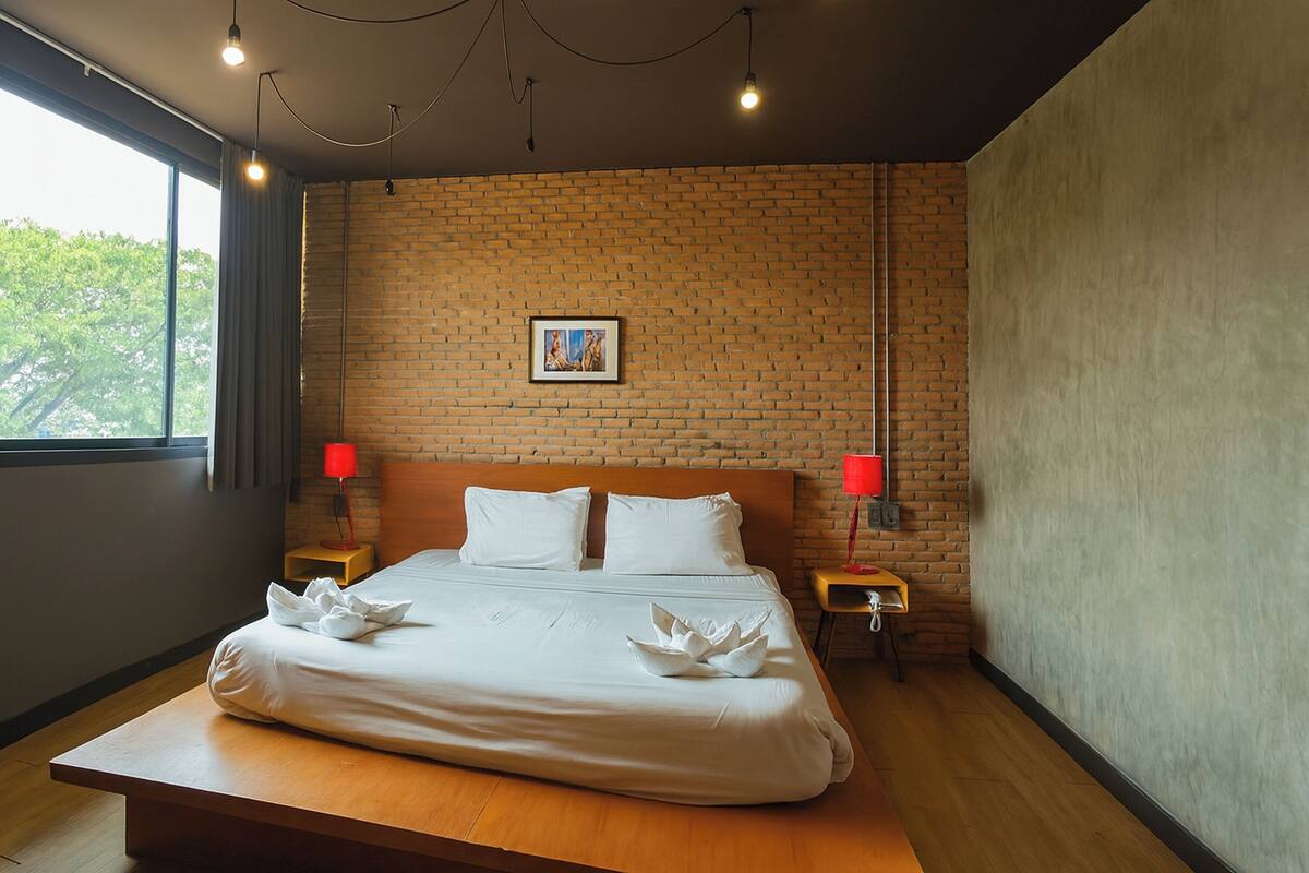 A hotel room with a large bed, two bedside tables, a brick wall, and a window.