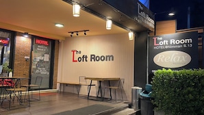 An outdoor seating area with tables and chairs, a sign for 'The Loft Room' hotel, and a 'Relax Massage' advertisement. - The Loft Room Nimman (Chiang Mai)