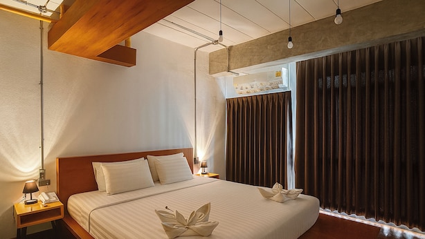 A hotel room with a large bed, wooden headboard, bedside tables with lamps, and a window with curtains. - The Loft Room Nimman (Chiang Mai)