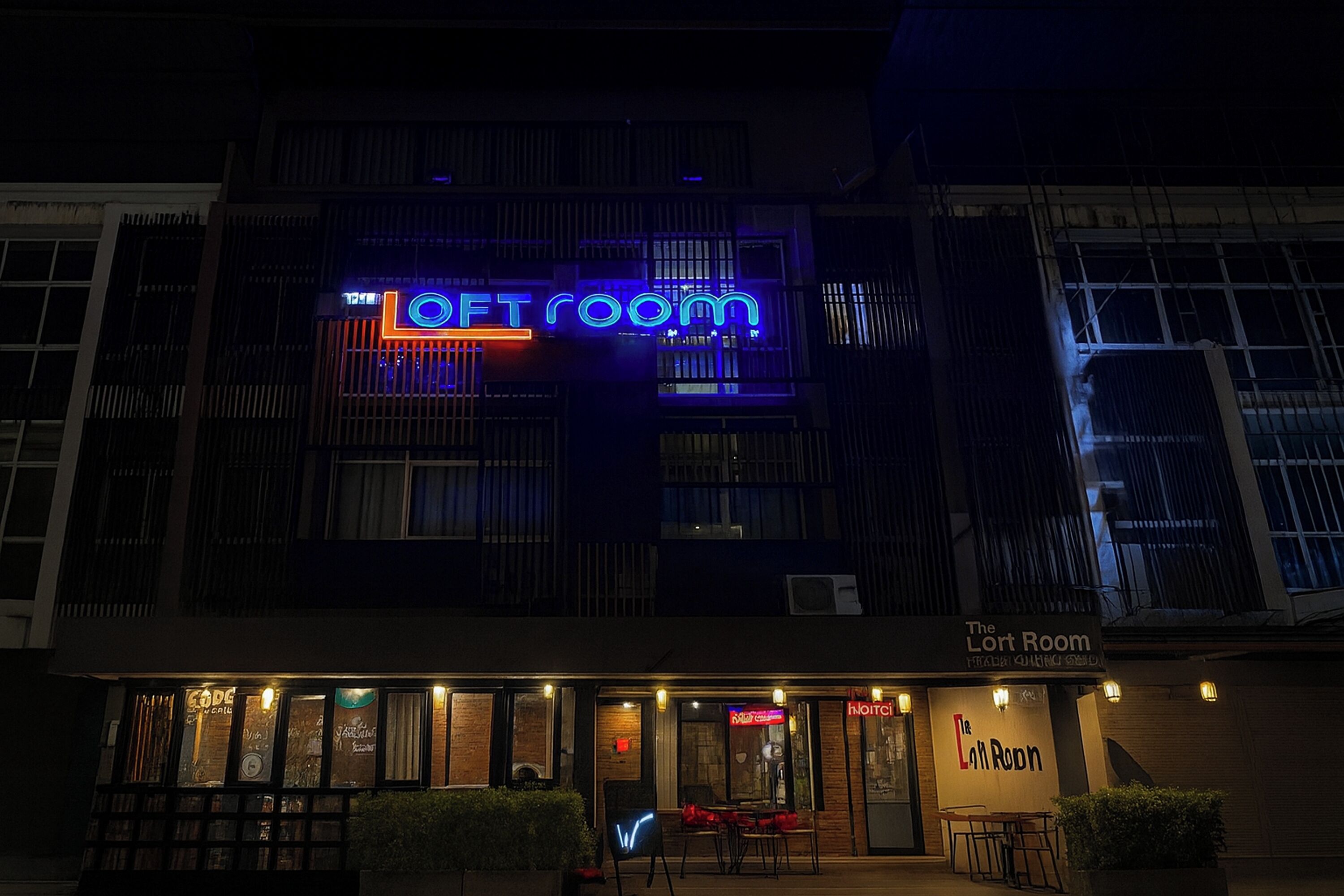 Un edificio con un letrero de neón que dice "LOFT room" y un cartel con la inscripción "The Loft Room" debajo.
