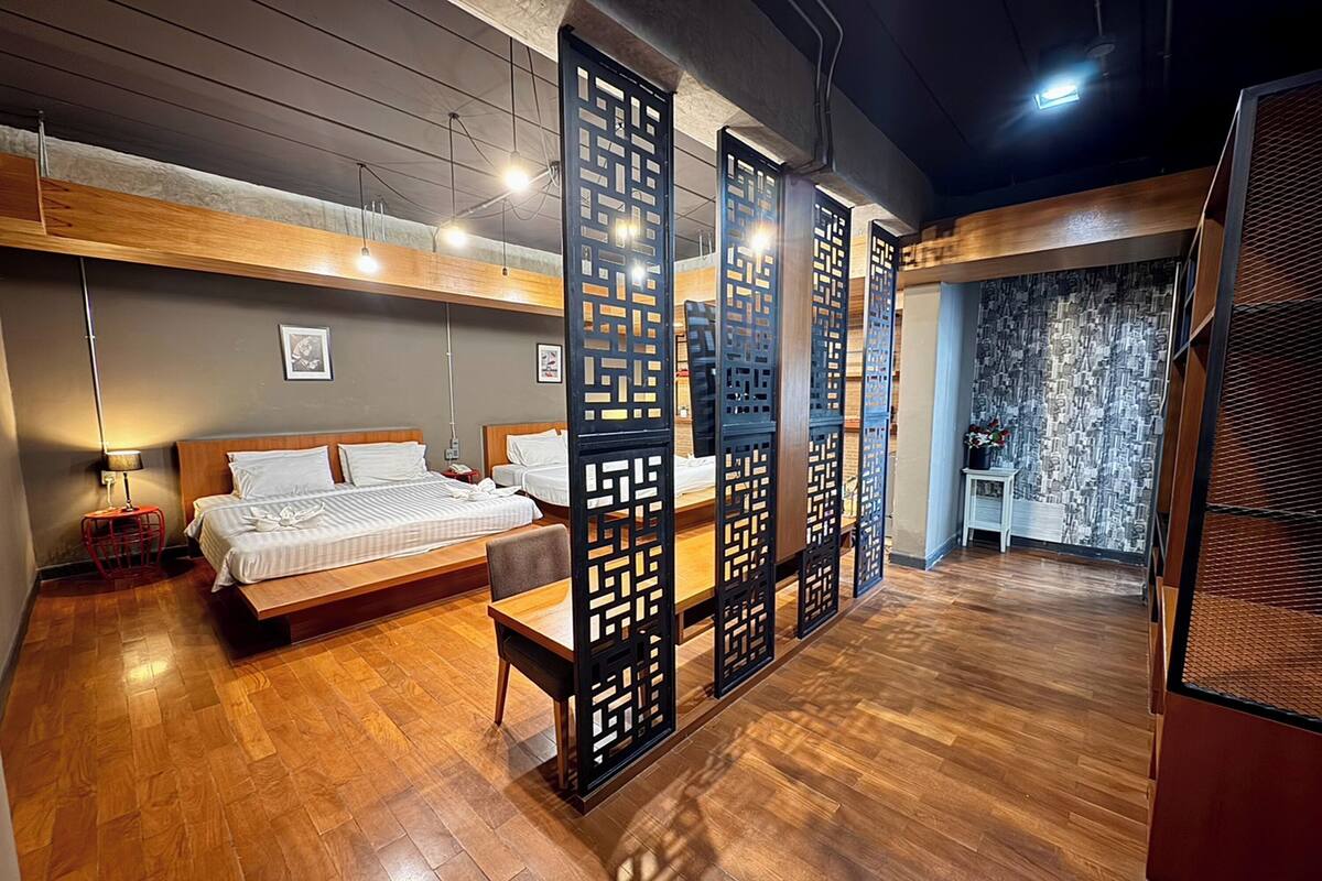 A modern hotel room with a wooden floor, a bed with white linens, a desk, and a decorative screen.