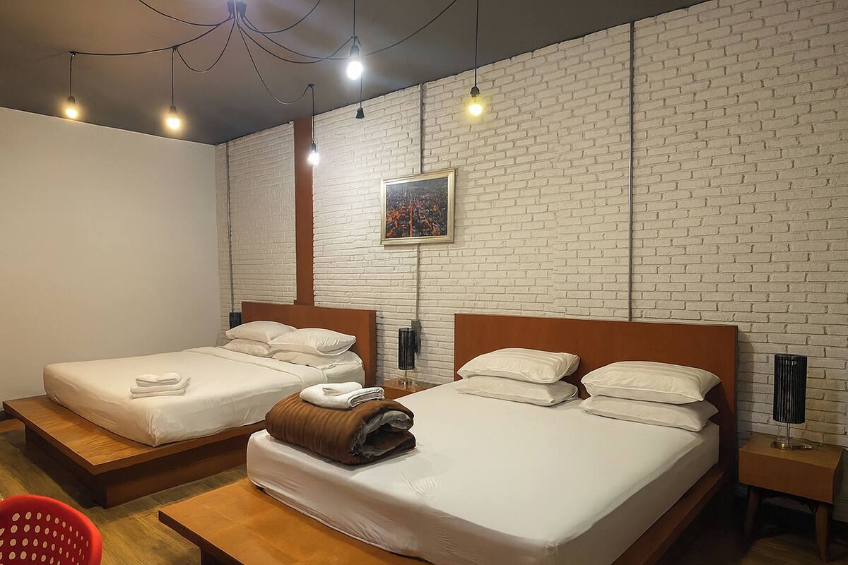 A hotel room with two beds, a brick wall, a framed picture, and a red chair.