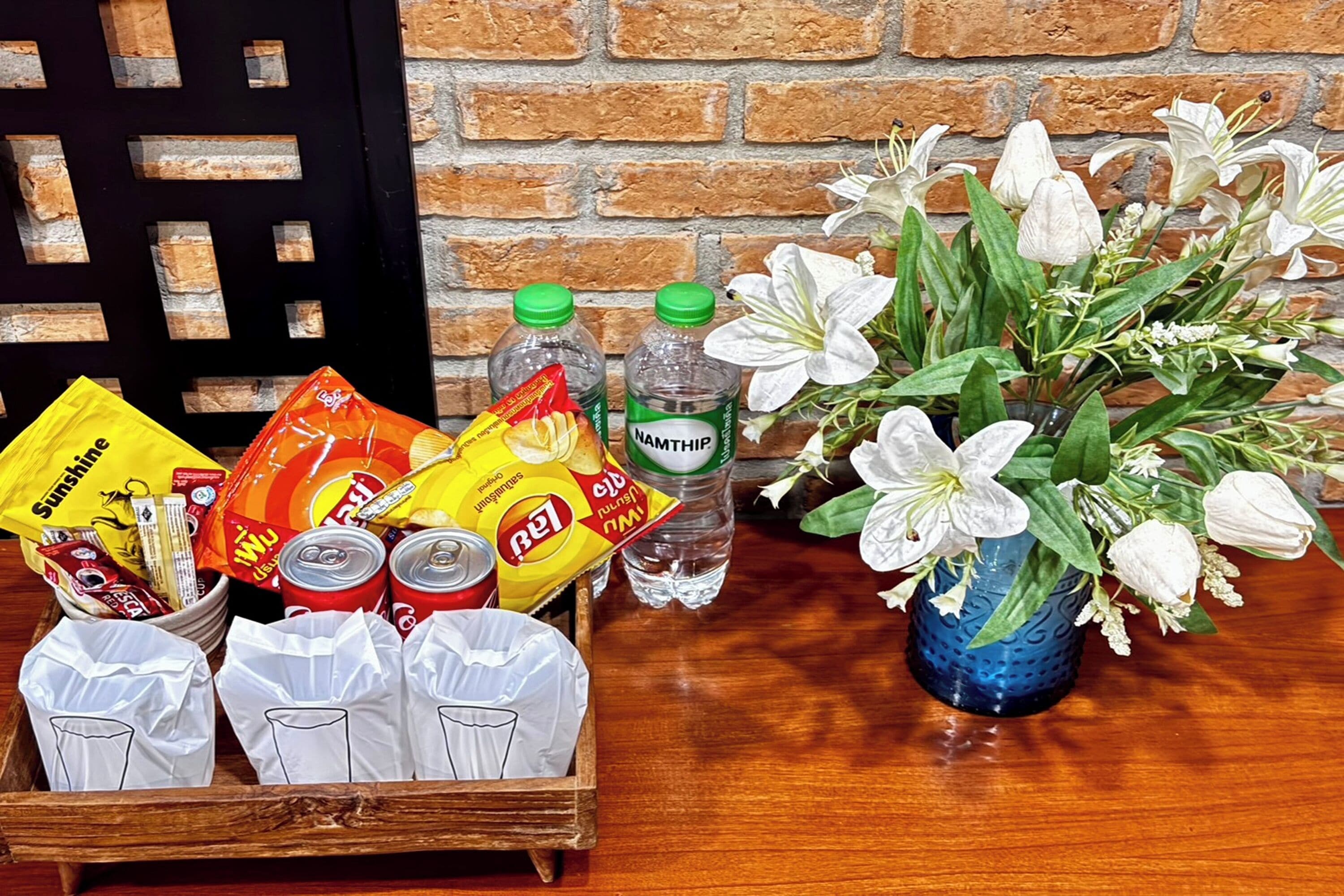 Una caja de madera con aperitivos, bebidas y un jarrón de flores sobre una mesa.