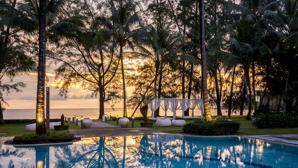 A pool area with a sunset view, surrounded by palm trees and a beach in the background. - The Anda Mani Khaolak Beachfront Villas (Thai Mueang)