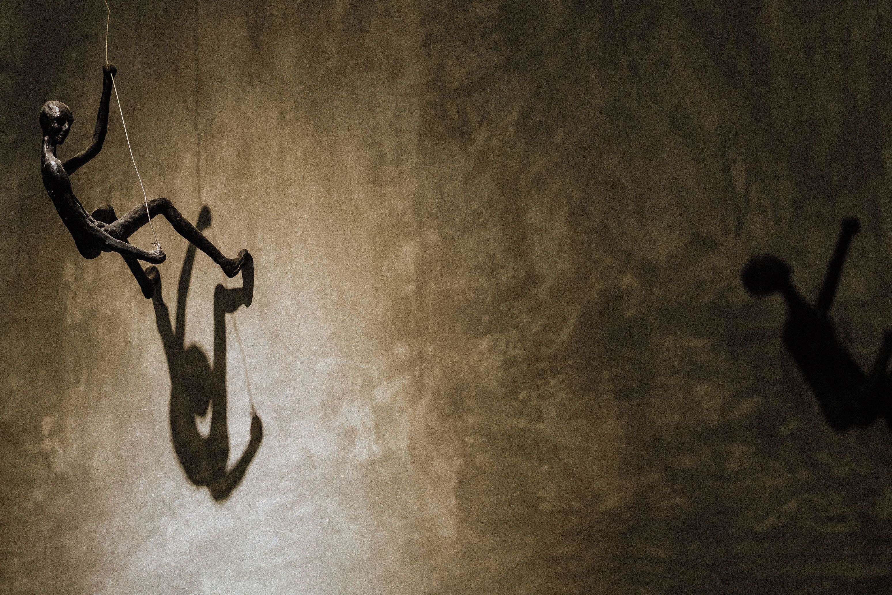 A person hanging from a rope against a textured wall.