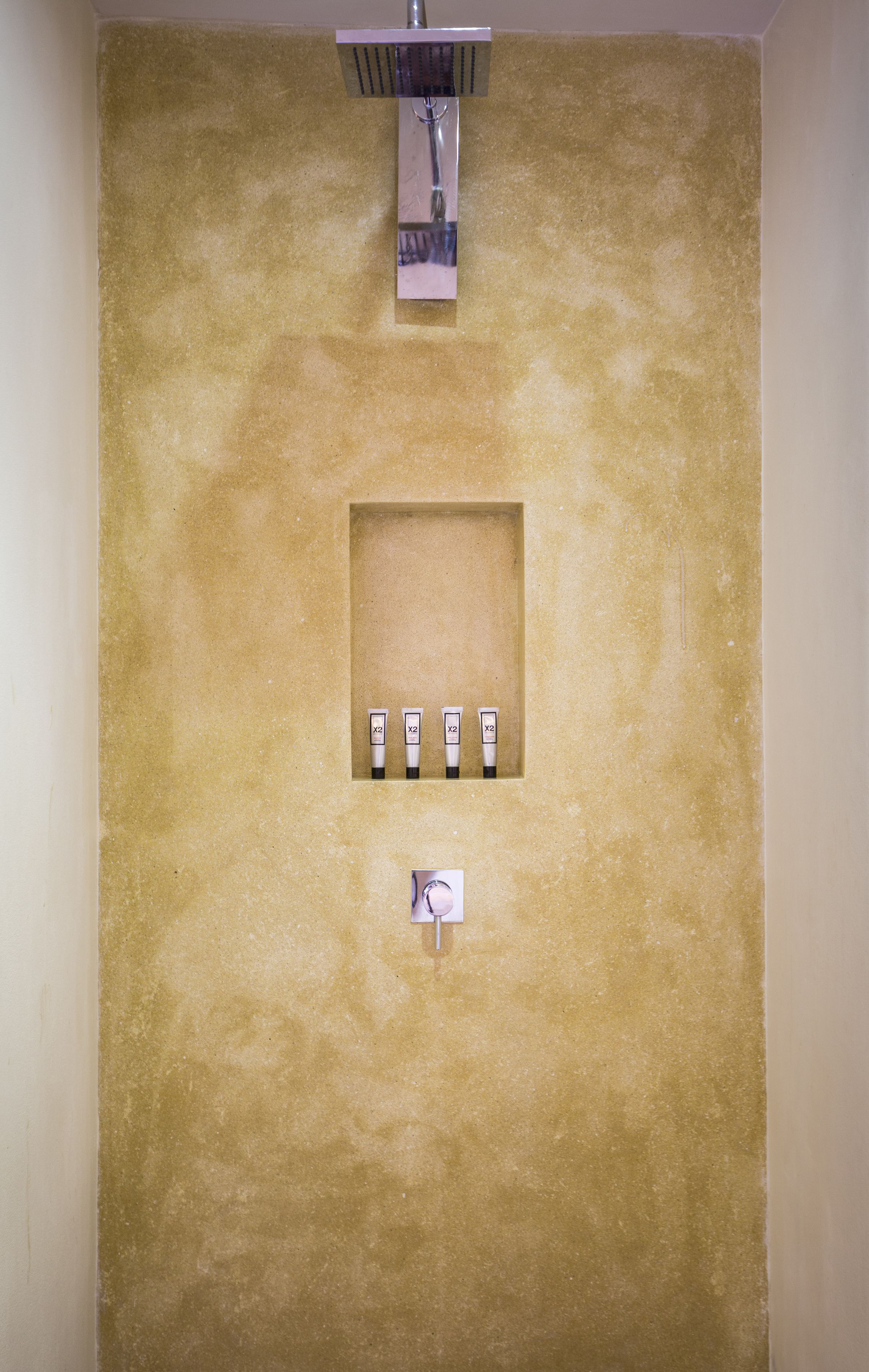 A bathroom with a beige textured wall, a square mirror, and four toiletries arranged in a row.