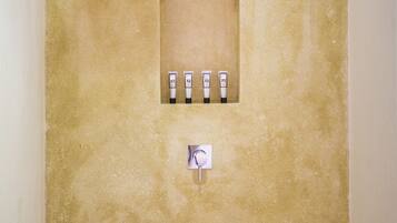 A bathroom with a beige textured wall, a square mirror, and four toiletries arranged in a row.