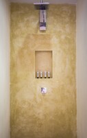 Un baño con una pared beige con textura, un espejo cuadrado y cuatro artículos de aseo dispuestos en fila.