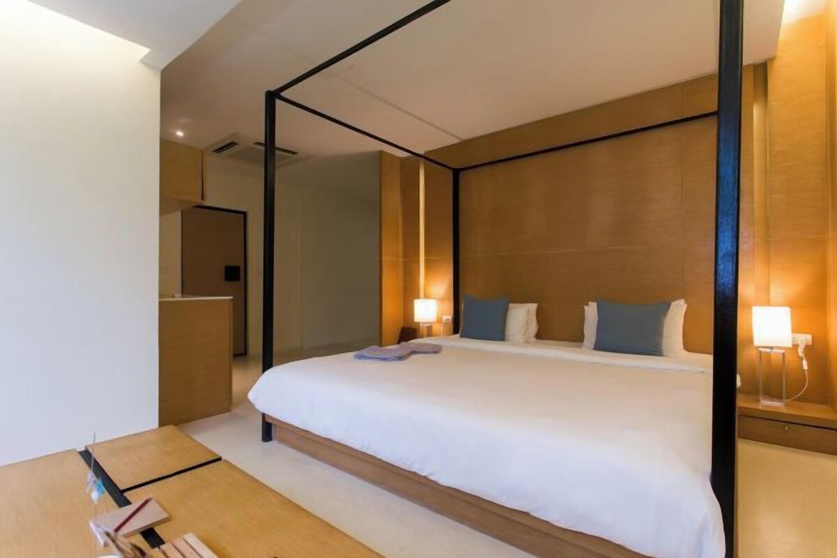 Une chambre d’hôtel moderne avec un grand lit, une tête de lit en bois, des lampes de chevet et une petite table en bois.