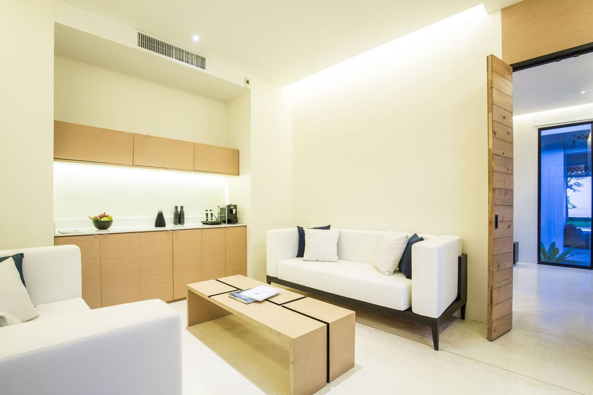 Una sala de estar moderna con un sofá blanco, una mesa de centro de madera y una cocina con armarios de madera y encimera.