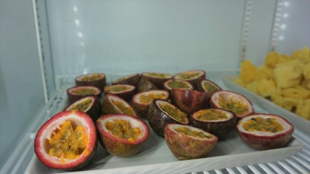 Vitrina refrigerada con fruta de la pasión en rodajas y mangos amarillos.