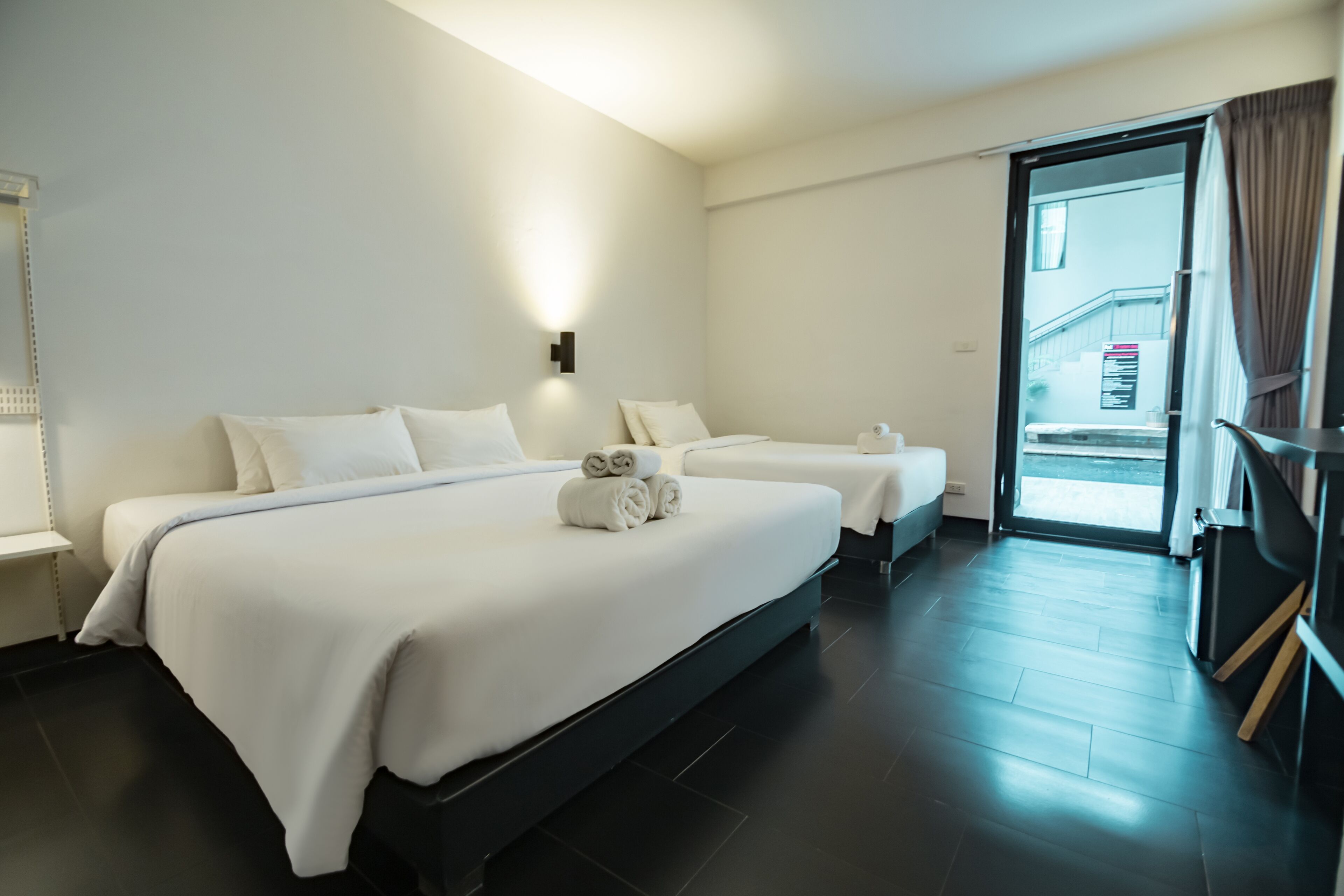 A hotel room with two beds, a large window, and a door leading to a balcony.