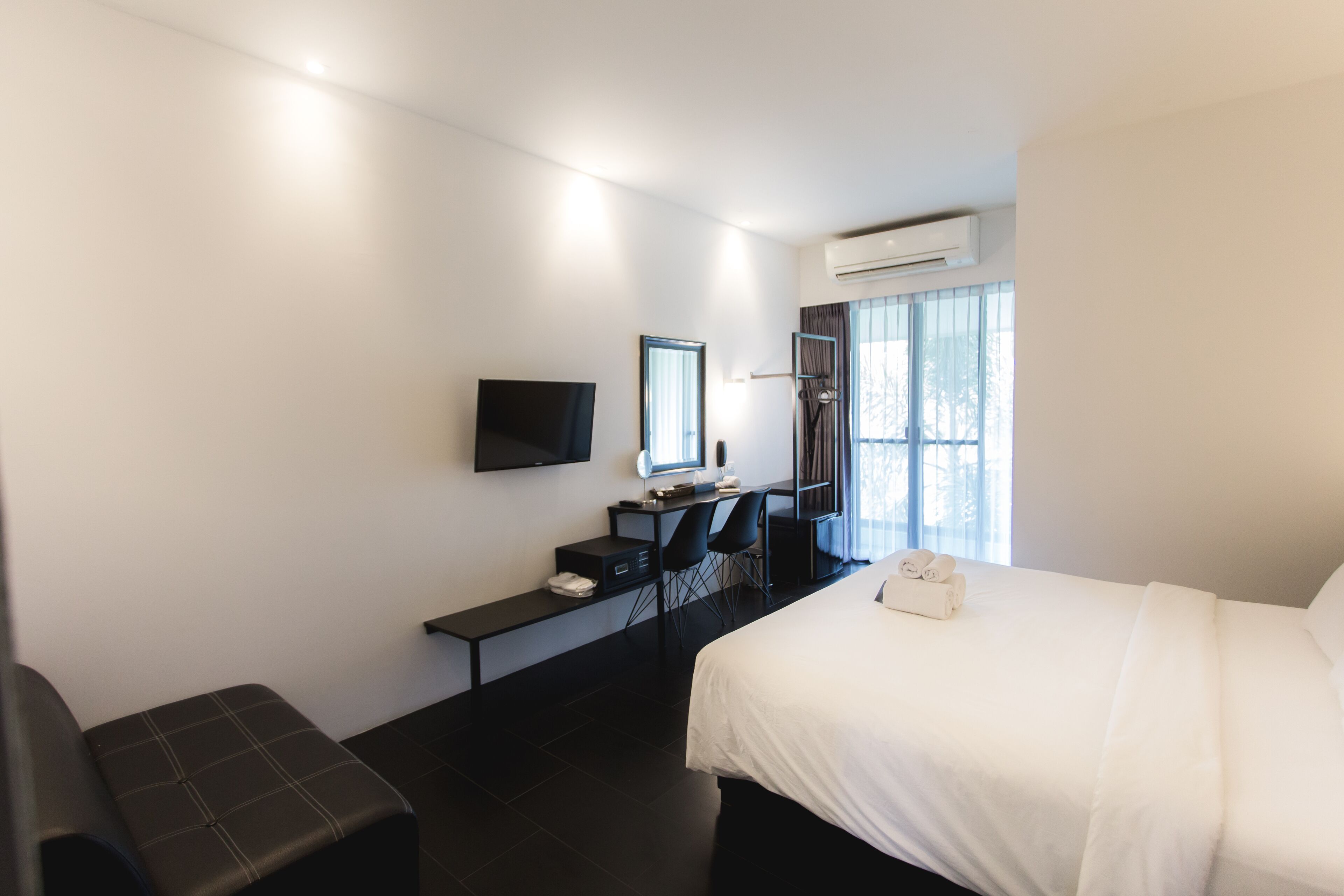 A hotel room with a bed, a desk with a chair, a television, and a window with curtains.