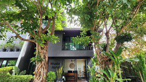 A modern hotel with a dark facade, large windows, and lush greenery surrounding the entrance. - iWualai Hotel (Chiang Mai)