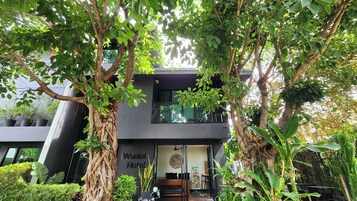 A modern hotel with a dark facade, large windows, and lush greenery surrounding the entrance.