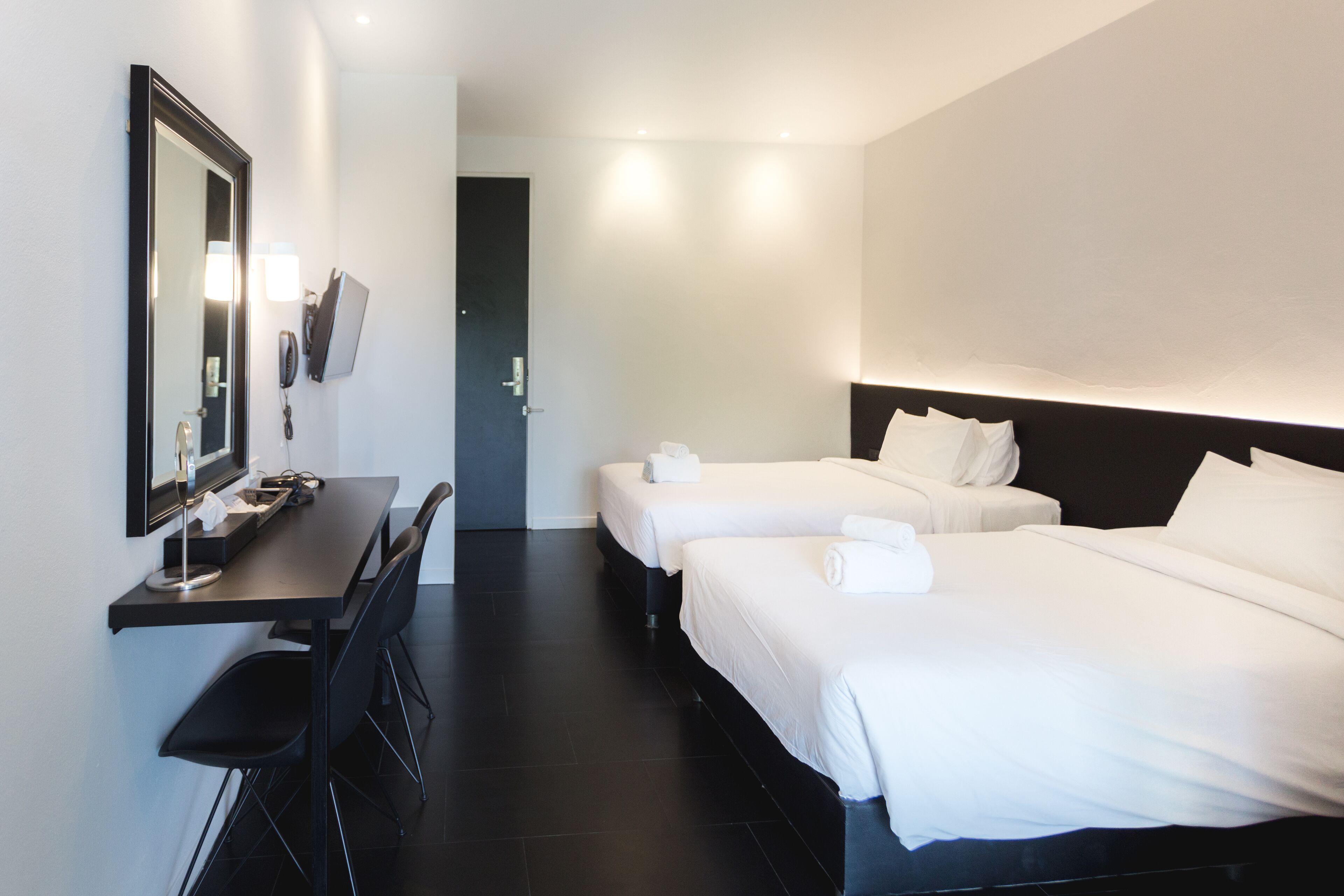 A hotel room with two beds, a desk, a chair, a mirror, and a phone on the wall.