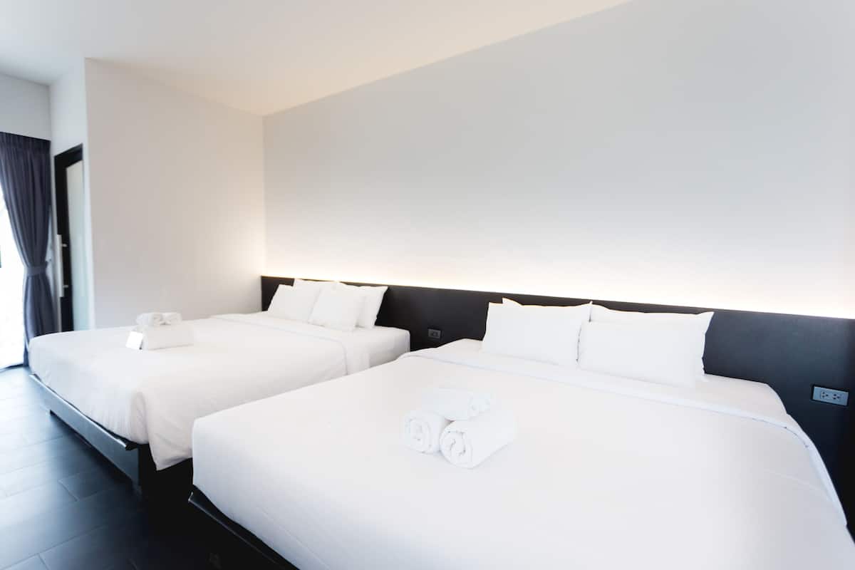 A hotel room with two beds, a dark headboard, and a large window with curtains.