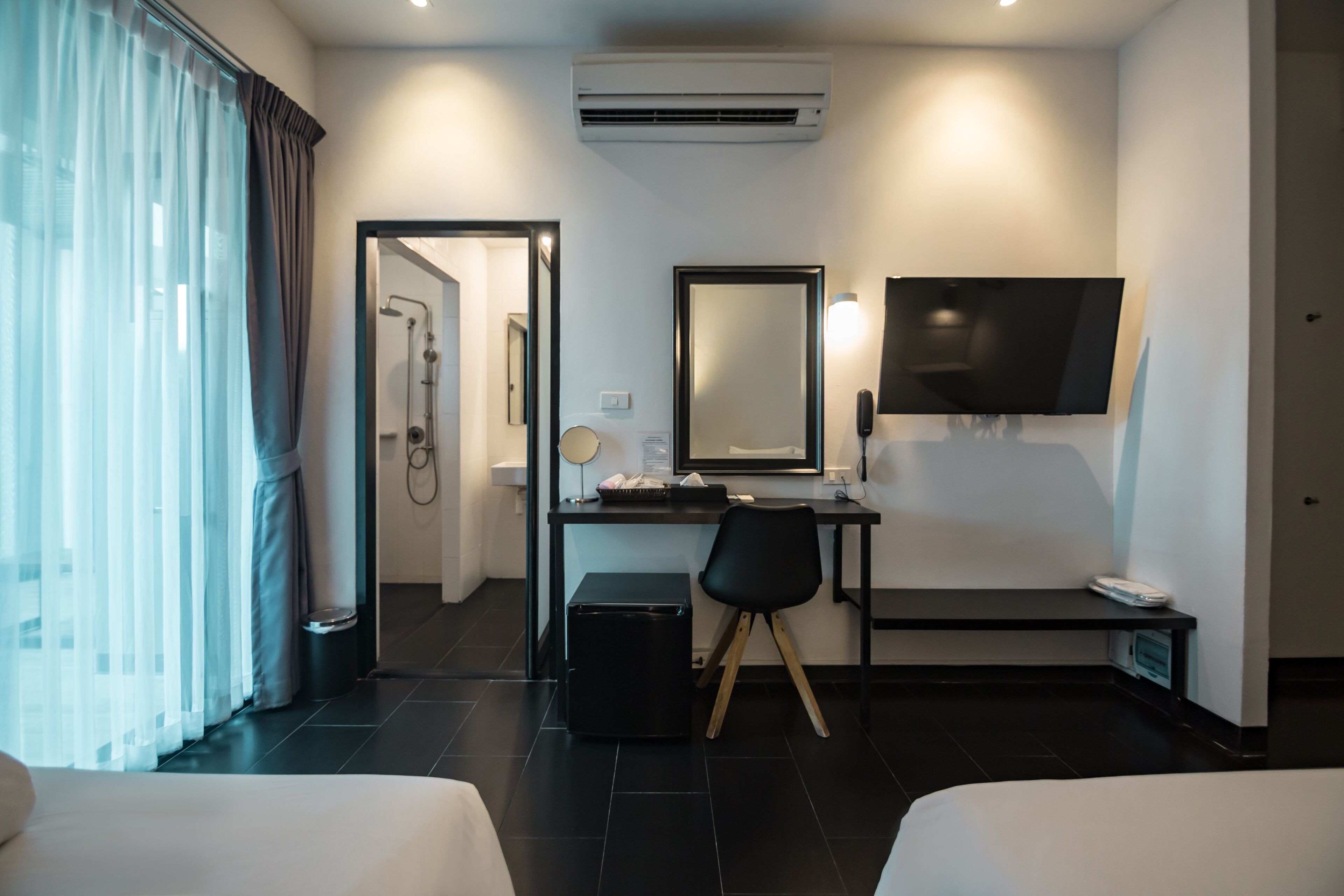 A hotel room with a bed, a desk with a chair, a TV, and a shower area.